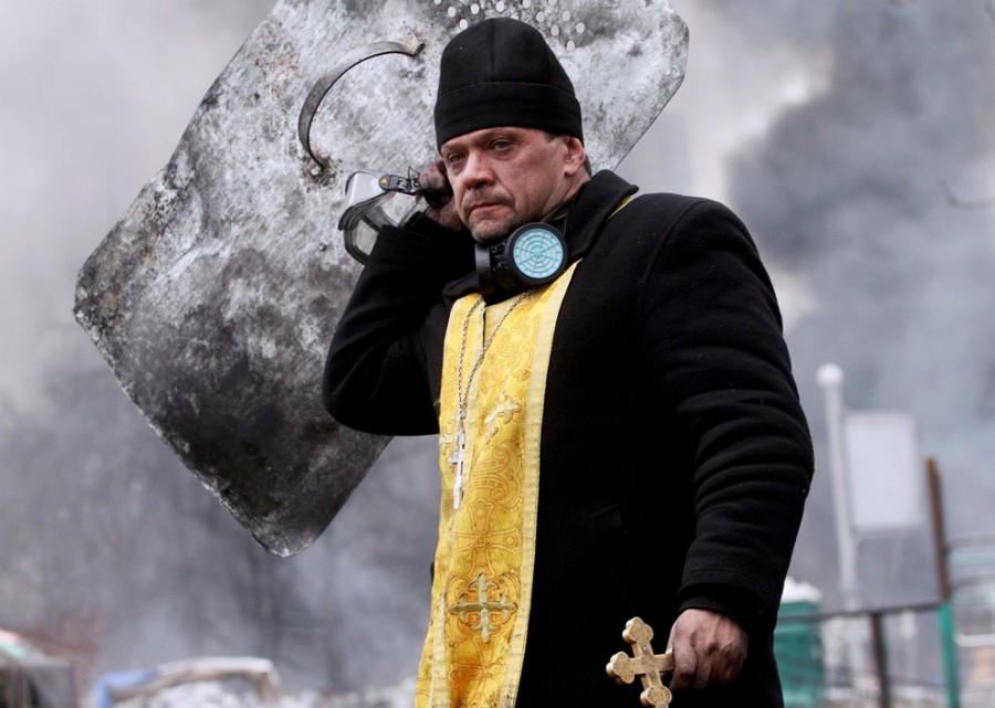 Priest holding a shield and cross during protests in Kiev courtesy theatlantic.com