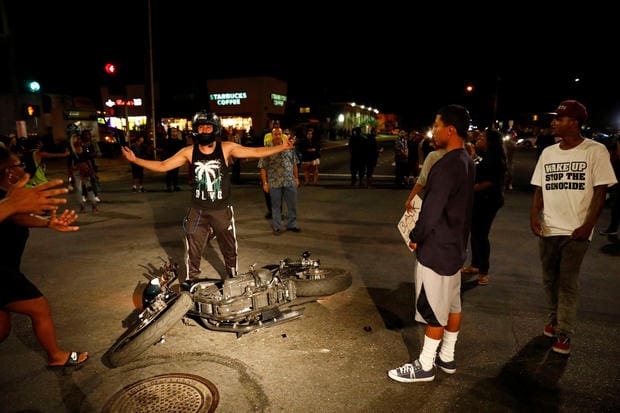 A motorcyclist reacts upon crashing his bike after he was pulled off of it by people protesting the death of Alfred Olango, who was shot by El Cajon police Tuesday, by blocking traffic near the parking lot where Olango was shot in El Cajon, California, U.S. September 29, 2016. Other protesters intervened before a full on fight broke out, calming the situation and paying the man for damage to his motorcycle. REUTERS/Patrick T. Fallon
